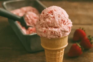 A bowl of creamy homemade strawberry ice cream with fresh strawberries on top.